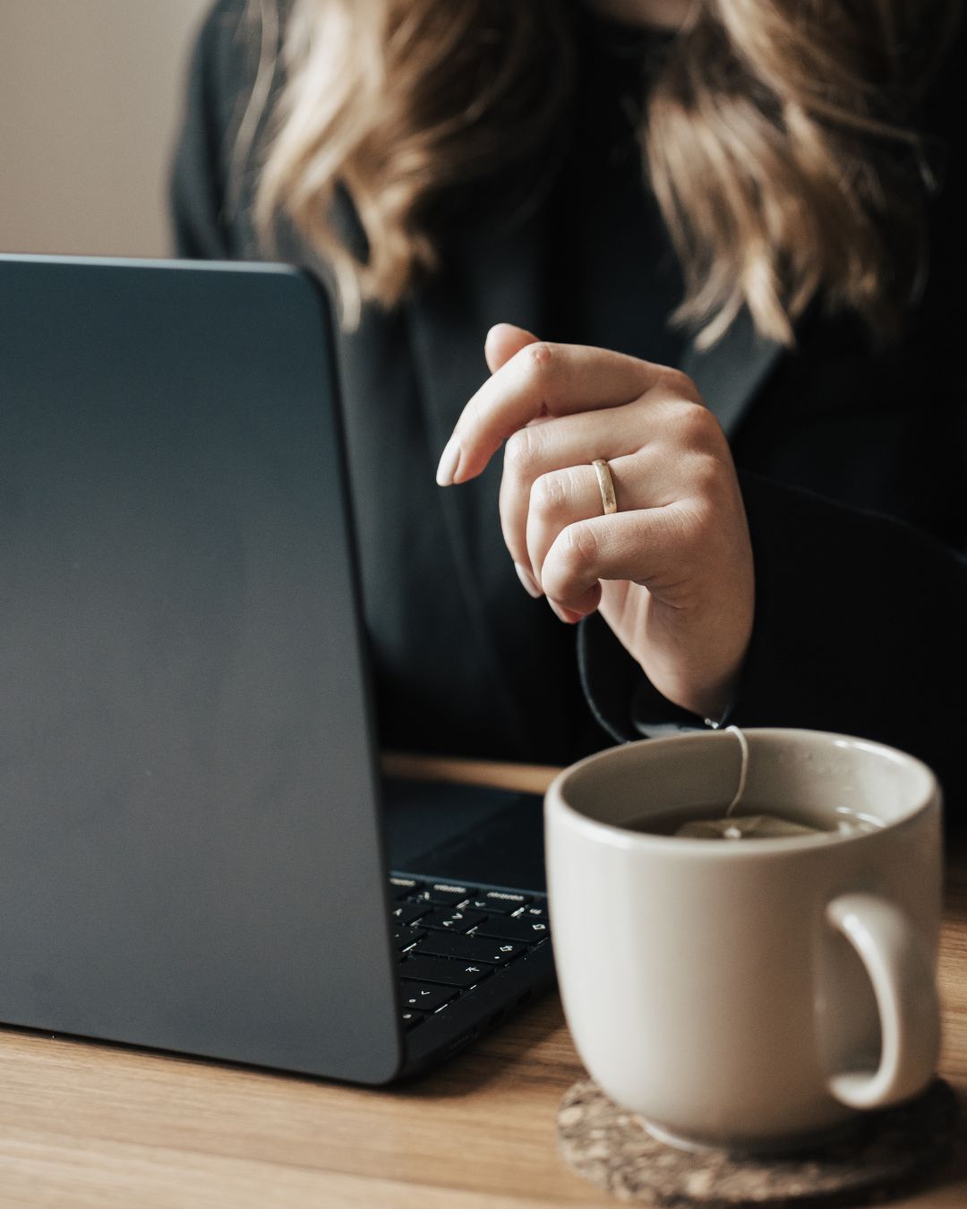 Es ist der Ausschnitt eines Laptops sowie eine Hand und eine Tasse Tee zu sehen
