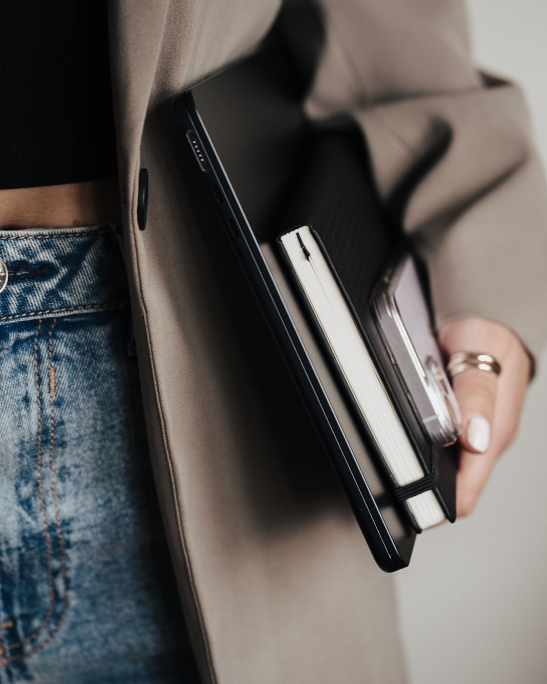 Eine Nahaufnahme von einer Person, die einen Laptop, ihr Handy und ein Buch in der Hand hält